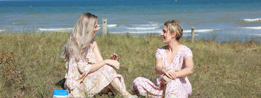 two women sitting on grass near the ocean chatting