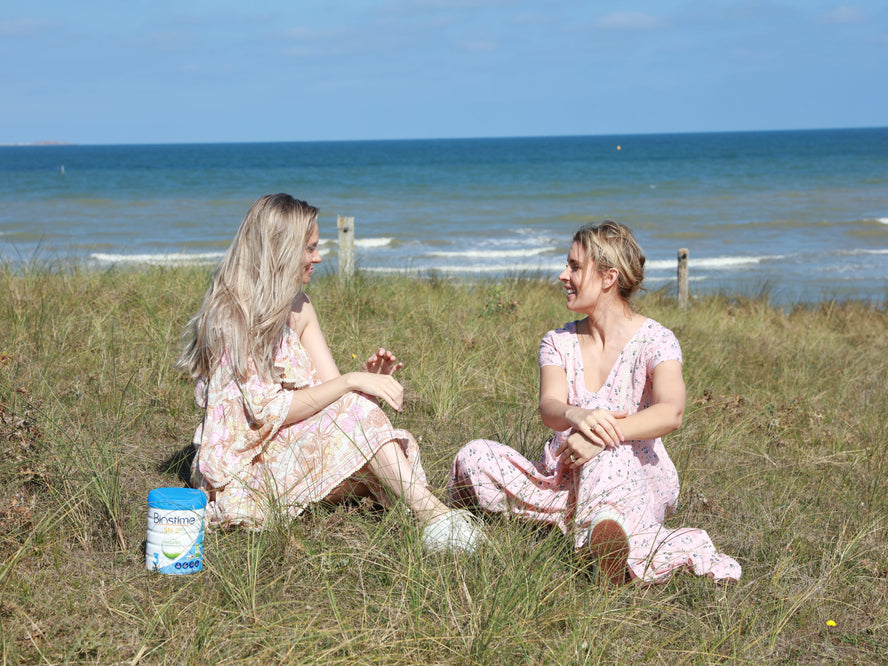 two women sitting on grass near the ocean chatting