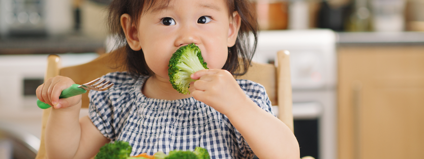 toddler girl sitting at a table eating fresh fruit and vegetables
