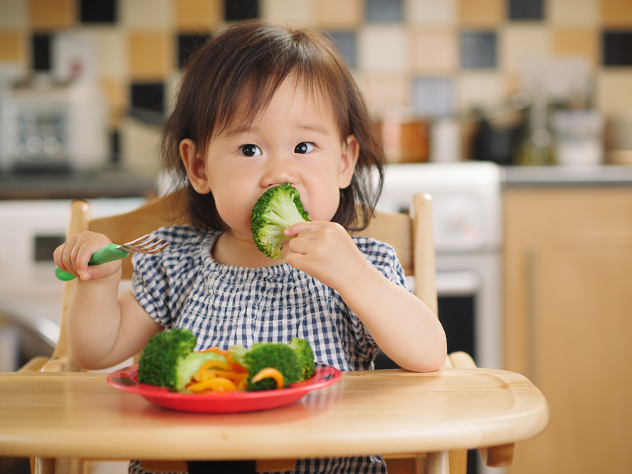 toddler girl sitting at a table eating fresh fruit and vegetables