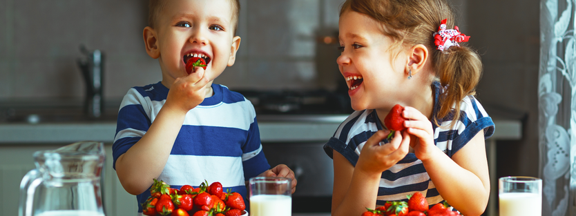 boy and girl toddler laughing with strawberries and milk