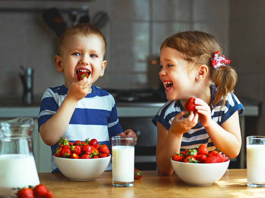 boy and girl toddler laughing with strawberries and milk