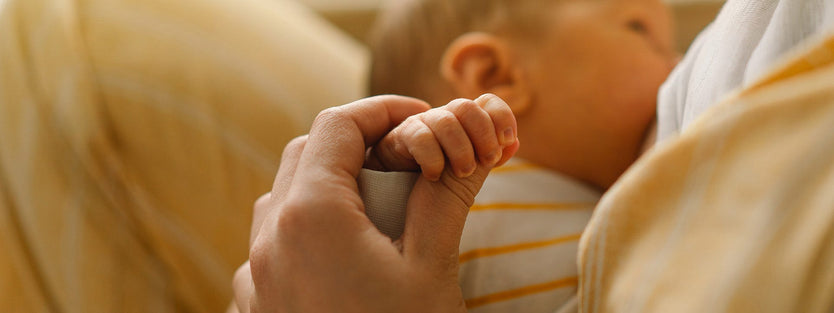 Mom breastfeeding newborn while holding baby's hand