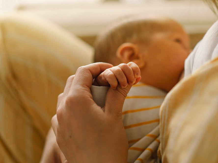 Mom breastfeeding newborn while holding baby's hand