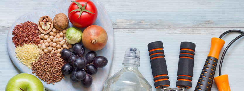 Fruit and nuts on a heart shaped plate next to a bottle of water, skipping rope and a hand grip