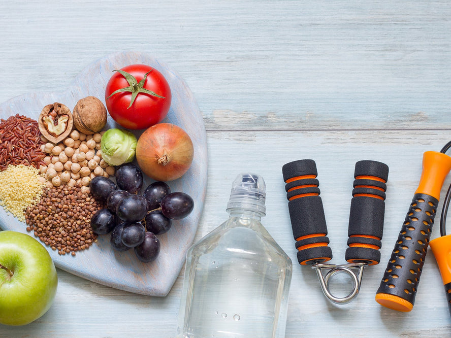 Fruit and nuts on a heart shaped plate next to a bottle of water, skipping rope and a hand grip