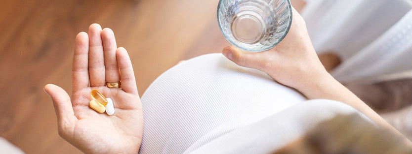 Pregnant woman holding vitamins in one hand and a glass of water in the other hand