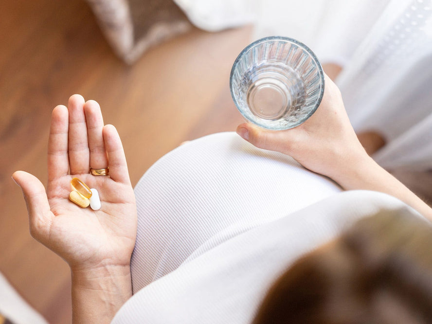 Pregnant woman holding vitamins in one hand and a glass of water in the other hand