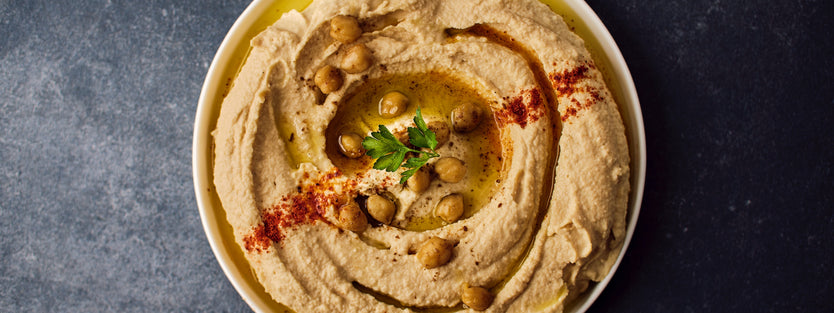 Bowl with hummus topped with whole chickpeas, paprika, oil and herbs