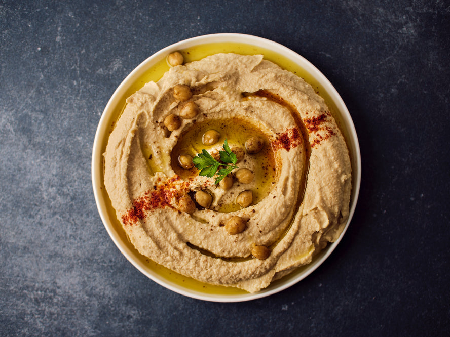 Bowl with hummus topped with whole chickpeas, paprika, oil and herbs
