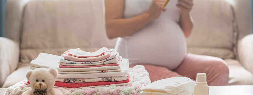 Folded baby clothes and nappies against a Pregnant woman with a notebook on her hands
