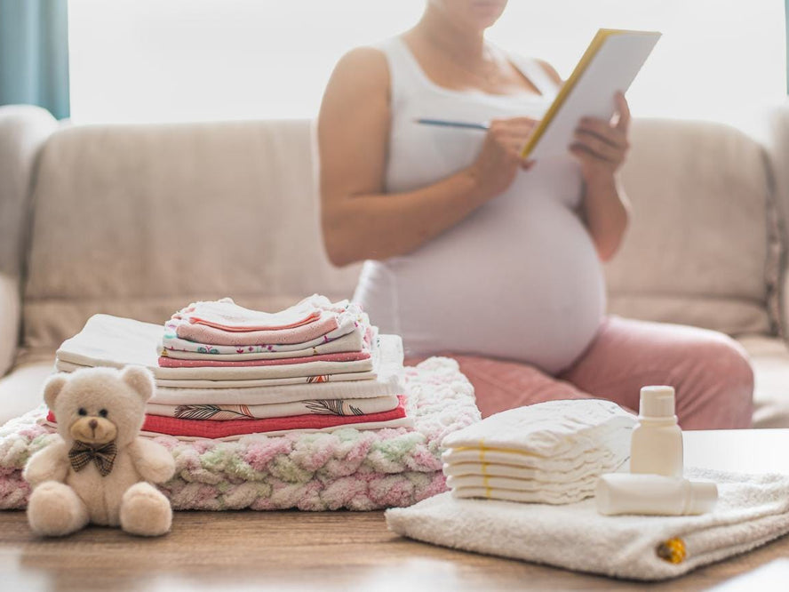 Folded baby clothes and nappies against a Pregnant woman with a notebook on her hands