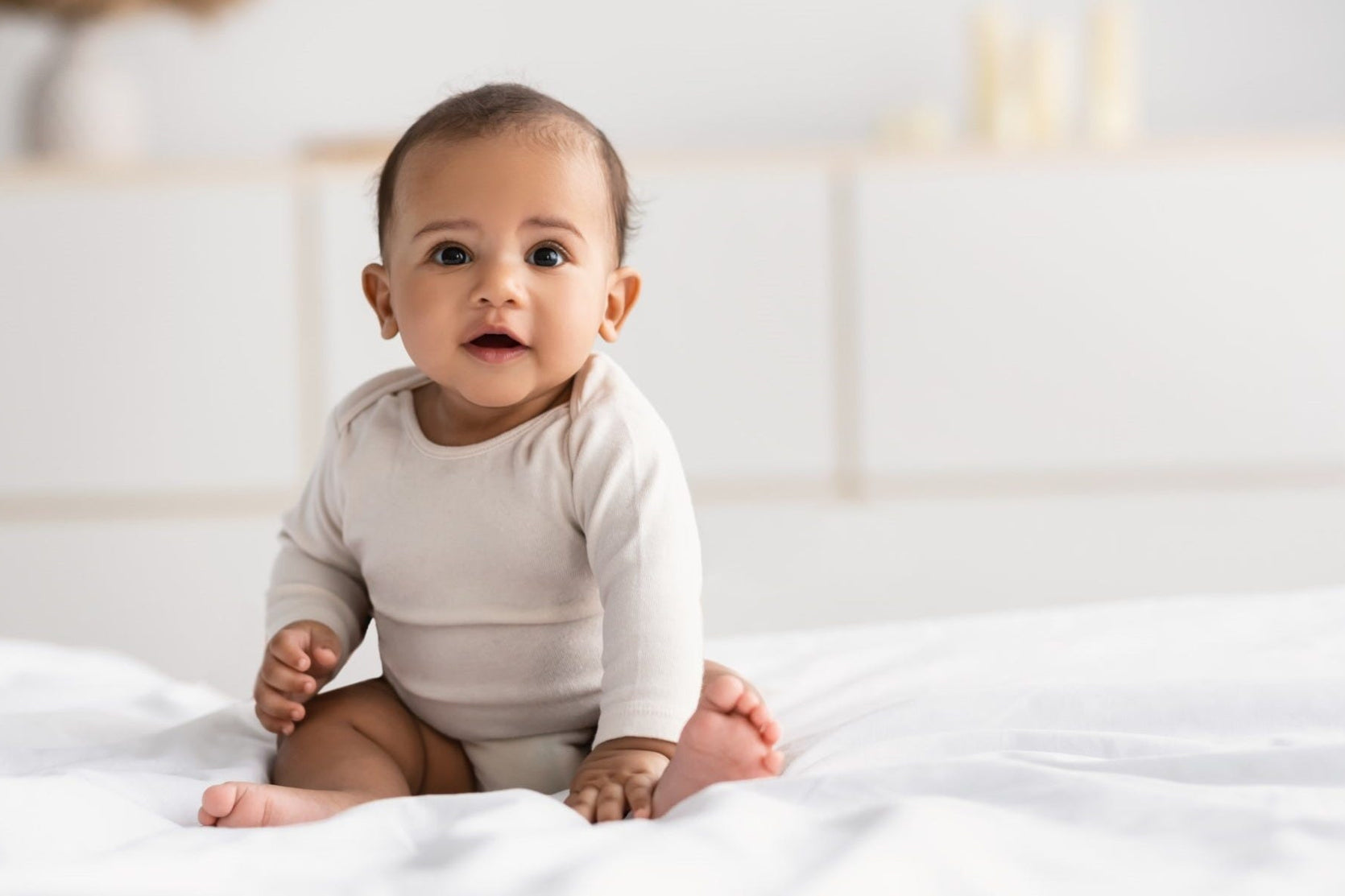 6-month-old Baby seating on a white blanket looking at the camera