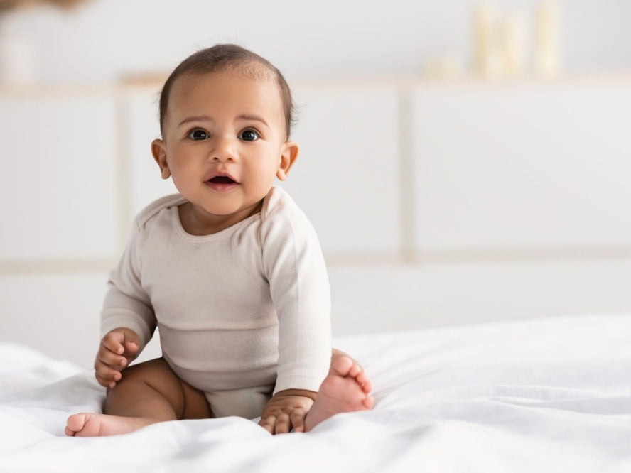 6-month-old Baby seating on a white blanket looking at the camera