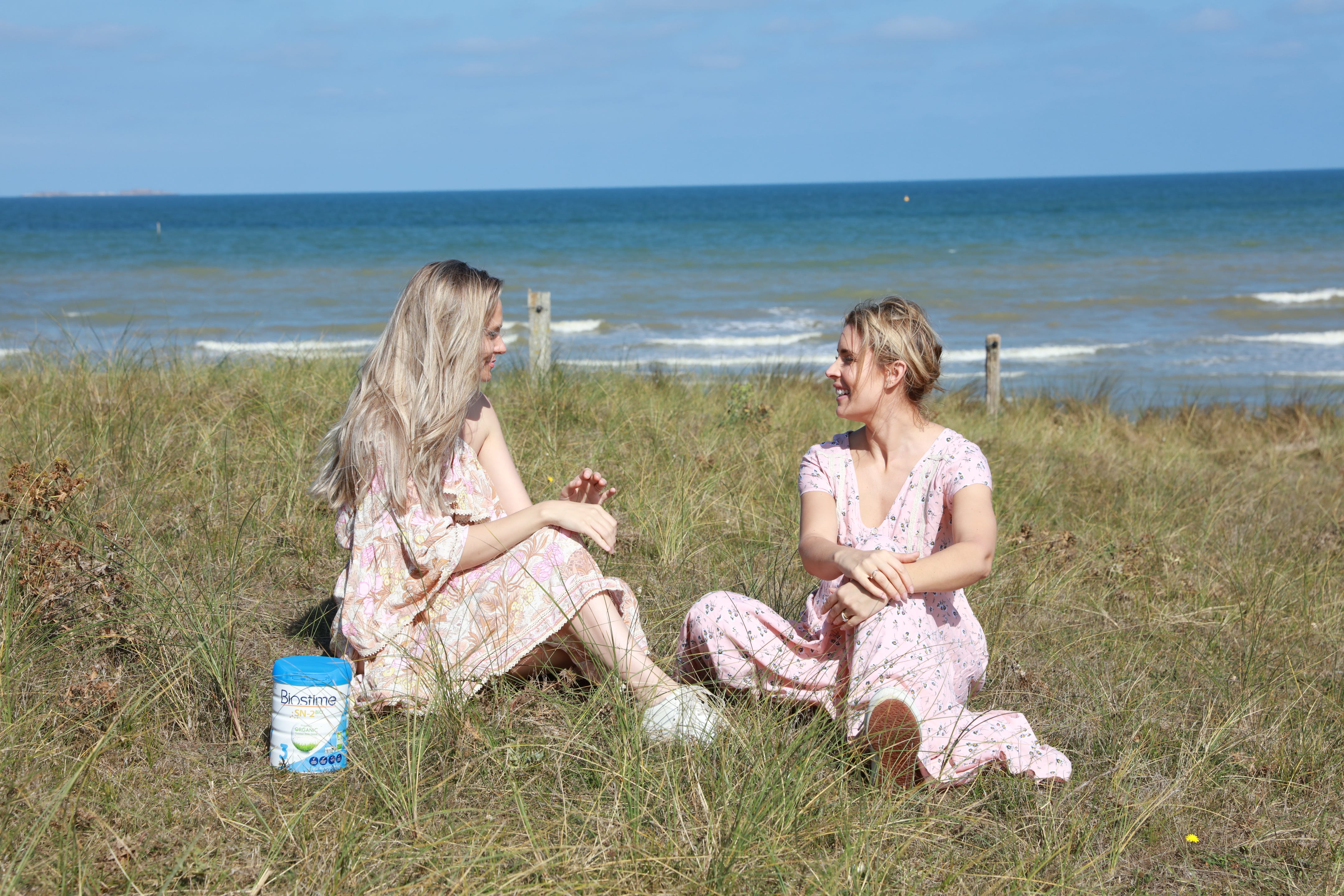two women sitting on grass near the ocean chatting 