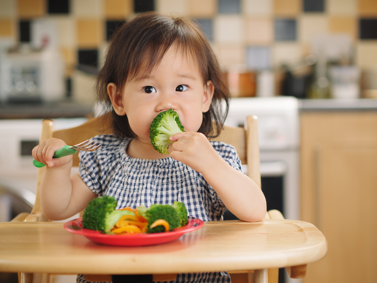 toddler girl sitting at a table eating fresh fruit and vegetables