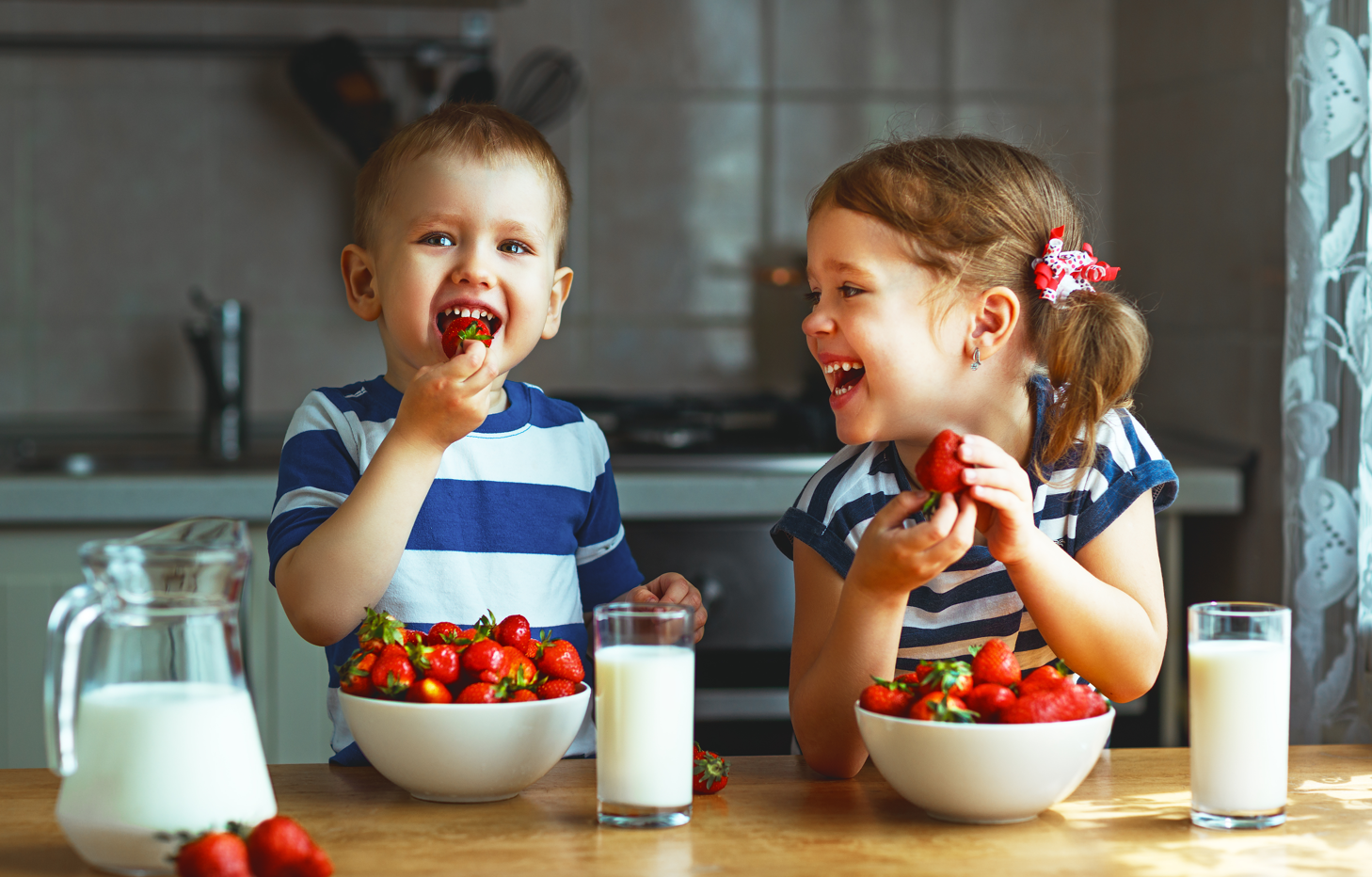 boy and girl toddler laughing with strawberries and milk 