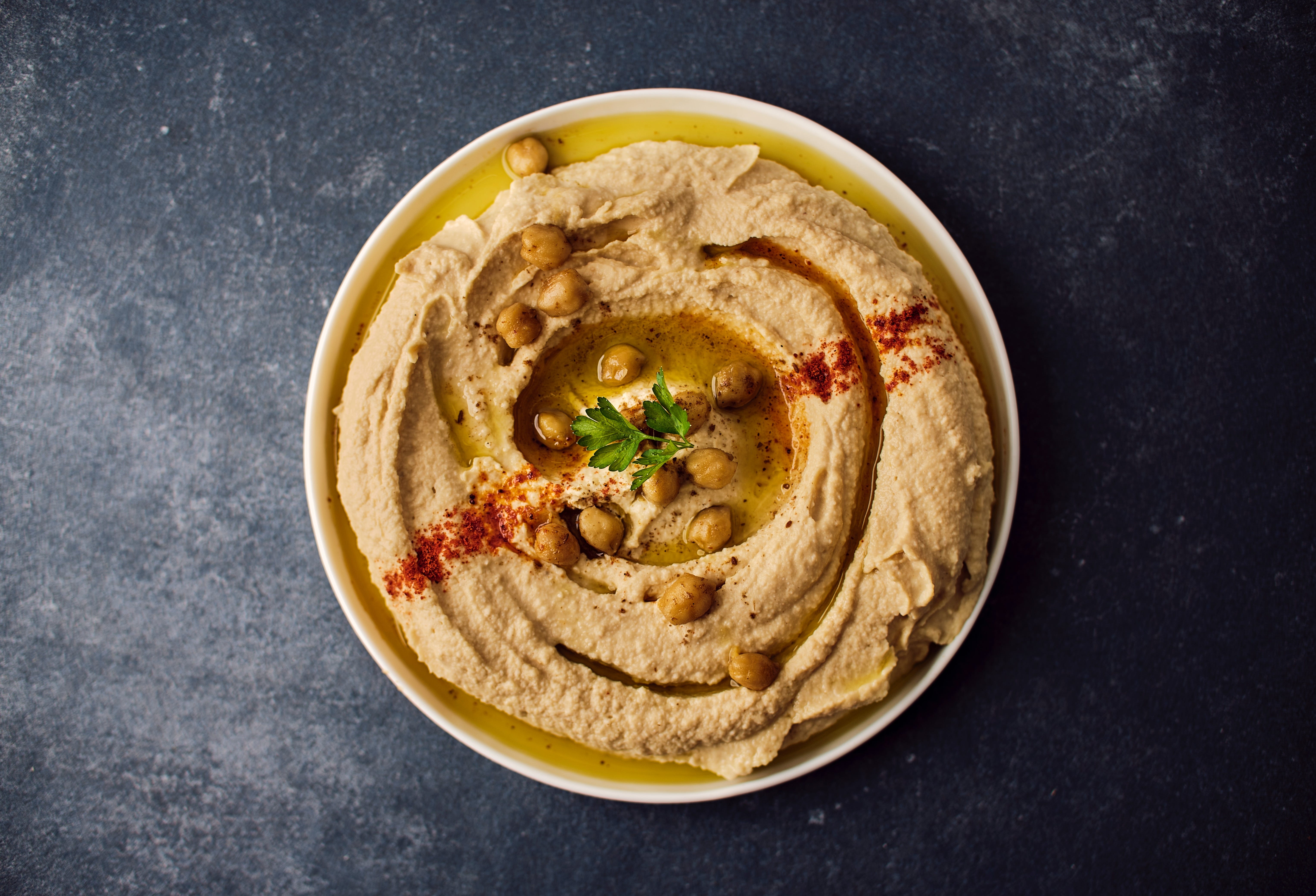 Bowl with hummus topped with whole chickpeas, paprika, oil and herbs