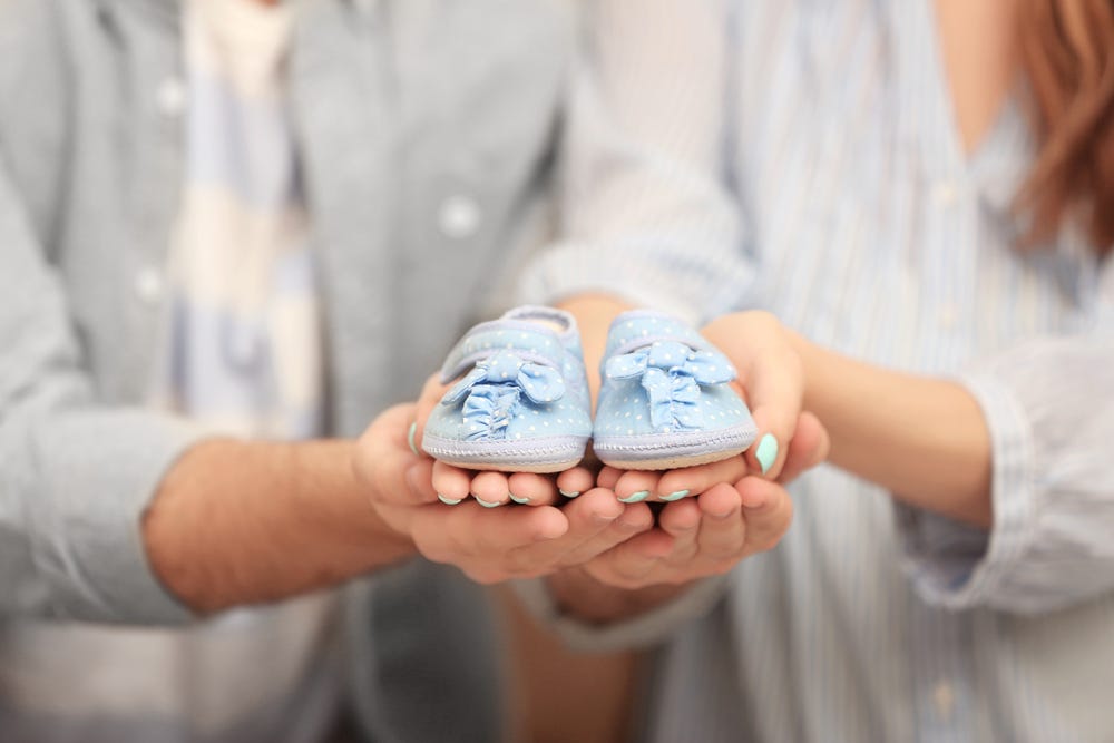 parents holding blue baby shoes
