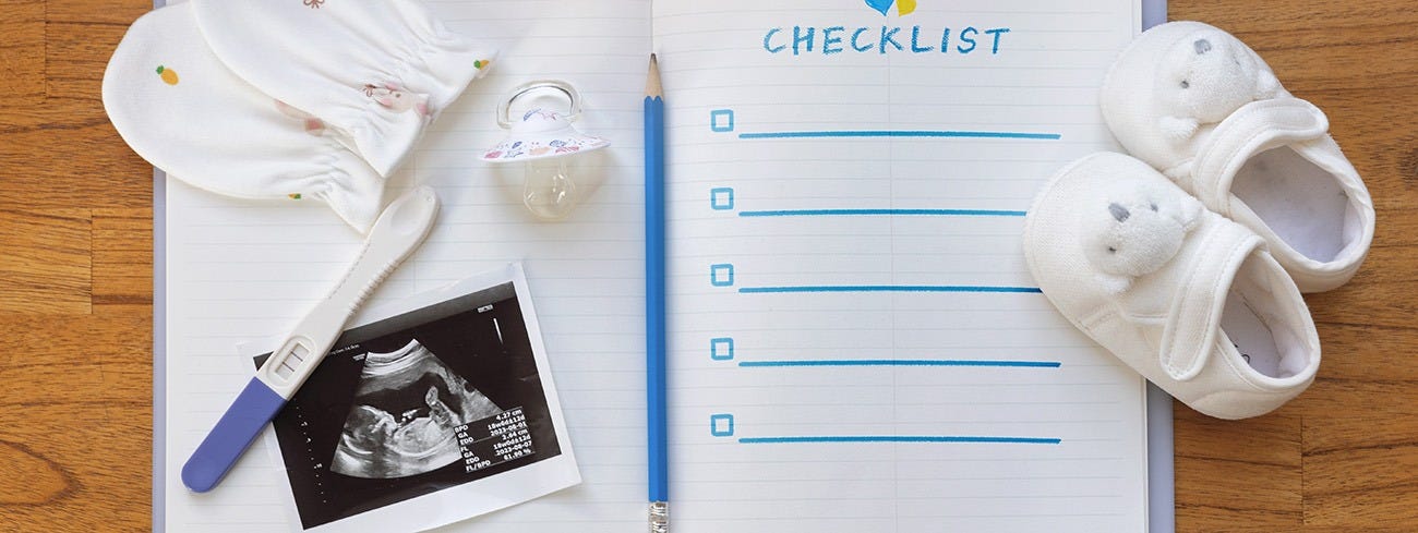 Open notebook with baby items on top including an ultrasound picture, baby shoes, mittens, and pregnancy test