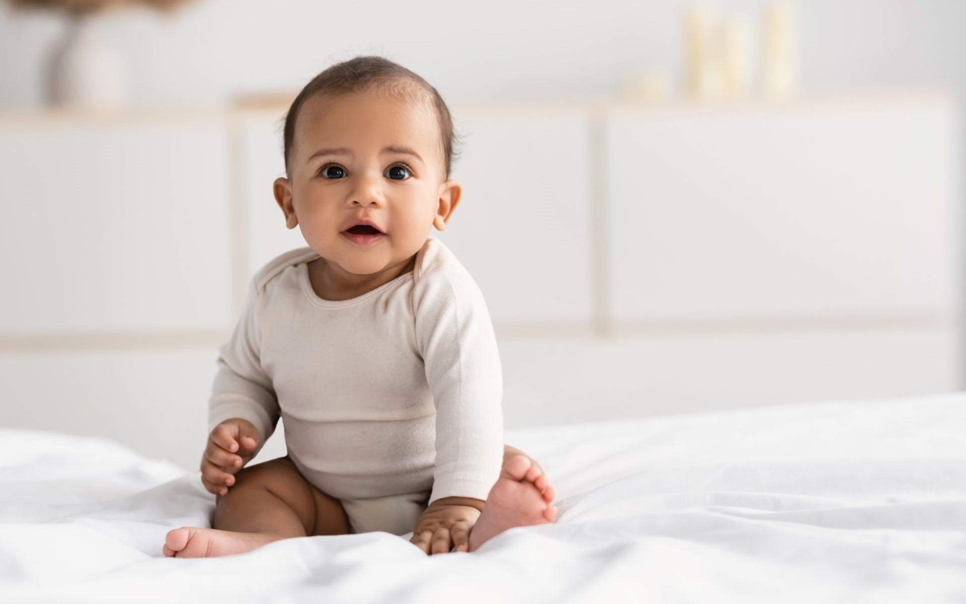 6-month-old Baby seating on a white blanket looking at the camera